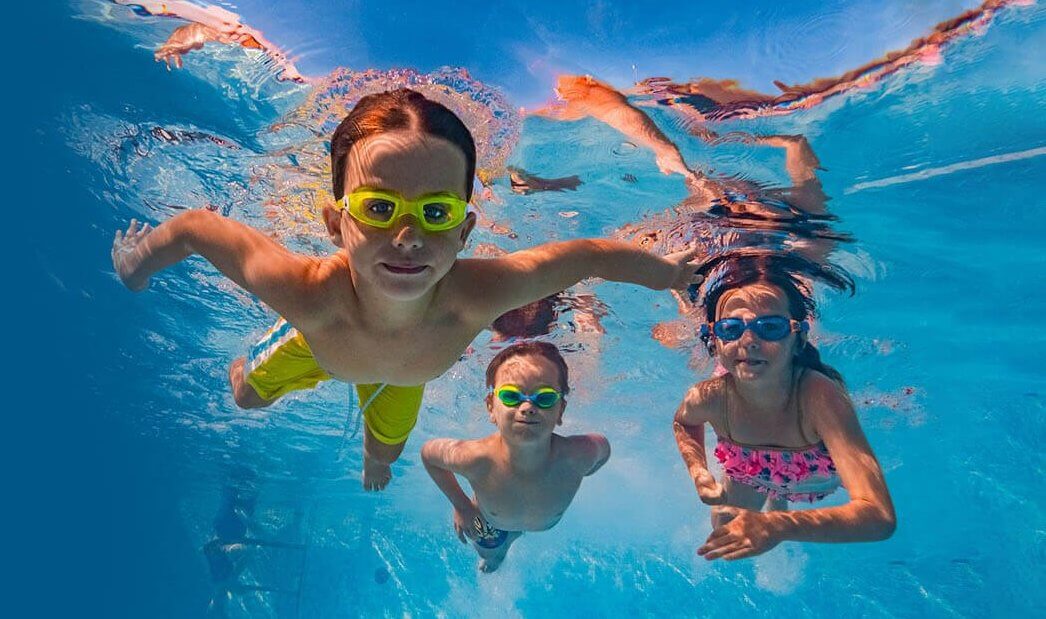3 kids swimming underwater in pool